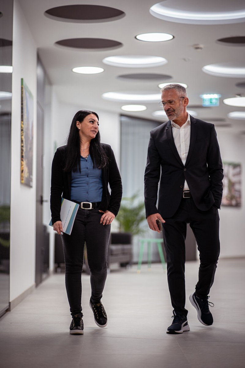 Zwei Personen im Gespräch in einem hellen Büroflur von AC AlphaConsult