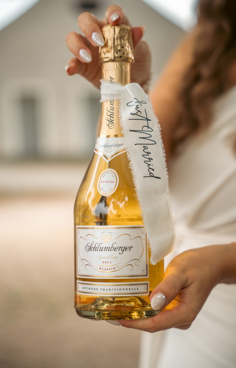 Hände der Braut halten eine Sektflasche mit einem Band mit der Aufschrift Just Married