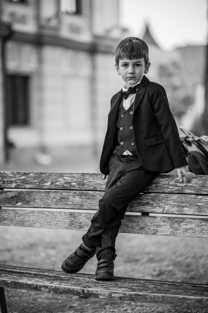 Schwarz-Weiß-Portrait eines jungen Hochzeitsgastes im Anzug auf einer Parkbank
